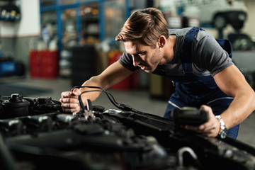 Auto mechanic using jumper cables while repairing car engine in a workshop.