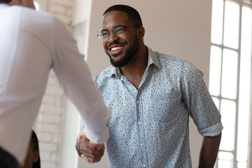 Joyful african american millennial worker shaking hands with colleague.