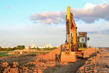 Obraz premium Large tracked excavator digs the ground for the foundation and construction of a new building in the city. Road repair, asphalt replacement, laying or replacement of underground sewer pipes - Image