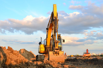 Obraz premium Large tracked excavator digs the ground for the foundation and construction of a new building in the city. Road repair, asphalt replacement, laying or replacement of underground sewer pipes - Image