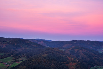 Naklejka na ściany i meble Germany, Red afterglow sky after sunset, aerial view above tree covered, forested mountains of black forest nature landscape in autumn