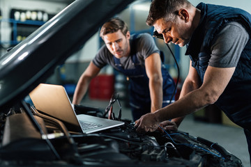 Two auto mechanic working on car diagnostic in auto repair shop.