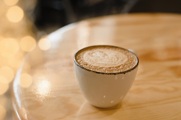Mug of hot cappuccino on a wooden table in a cafe with yellow garland lights