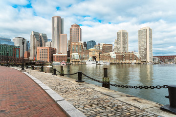 Boston skyline with a cobbled harborside path in foreground on a partly cloudy autumn morning