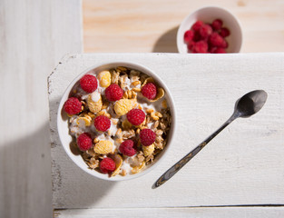 Bowl of granola with yogurt and raspberry on a white wooden background