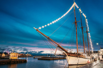 Helsinki, Finland. Old Wooden Sailing Vessel Ship Schooner Is Moored To The City Pier, Jetty. Unusual Cafe Restaurant In City Center In Lighting At Evening Or Night Illumination.