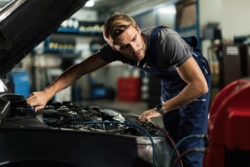 Young mechanic recharging air conditioner unit of a car in repair workshop.