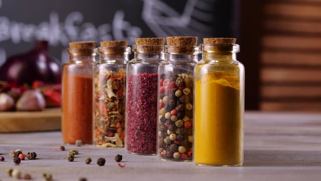 Different spices in glass bottles on the kitchen table. Nobody in the frame. Focus sliding to foreground hand puts papper. 4k.