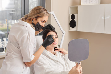 Close-up Of Surgeon Hands Drawing Correction Lines On Woman Face With Marker. Doctor's hand in black surgical glove marking women's face for cosmetic injections.