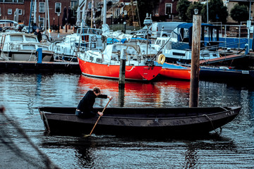 Fototapeta na wymiar boy fisherman rowing oars in a fishing boat among yachts moored in a port on the sea coast in the Netherlands in the early morning