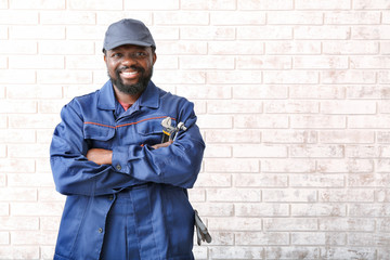 Naklejka premium African-American car mechanic near brick wall