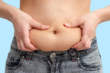 two hands woman holding excess fat on the stomach. on a blue background. front view
