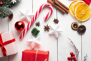 Beautiful Christmas composition on wooden white background with Christmas gift boxes, snowy fir branches, conifer cones, holiday decoration, caramel stick. New Year. Top view, copy space.