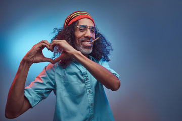 African Rastafarian smokes weed and showing heart symbol and shape with hands. Isolated on a blue...