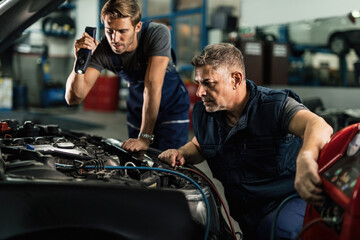 Auto mechanics charging car's AC unit in repair shop.