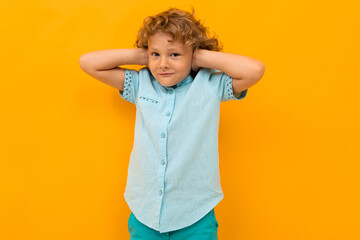 European red-haired boy in a light blue T-shirt closes his ears on a yellow studio background