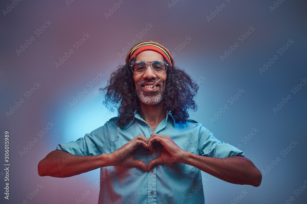 Wall mural African Rastafarian smokes weed and showing heart symbol and shape with hands. Isolated on a blue background.