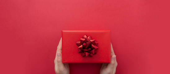 Female hands holding gift box with red ribbon bow isolated over flat lay background, copy space. Baner.
