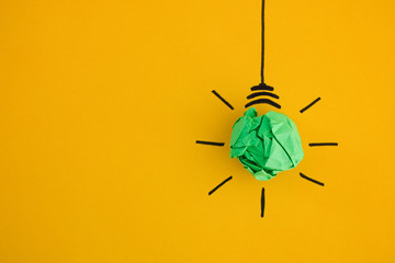 Crumpled green paper light bulb on yellow background