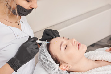 Obraz na płótnie Canvas Woman gets injection in her face. Beauty woman giving beauty injections. Young woman gets beauty facial injections in the cosmetology salon. Face aging injection. Aesthetic Medicine, Cosmetology