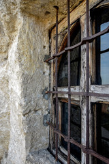 Wooden window of an ancient rock monastery. Protected by forged metal bars. Rusty iron. Close-up.