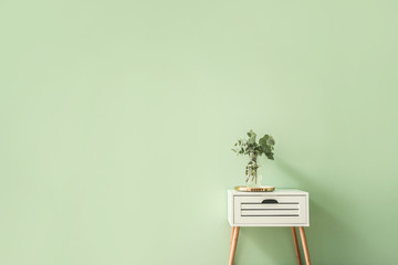 Stylish table with eucalyptus branches in vase on color background