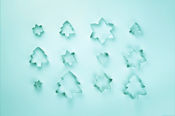 Christmas cookie cutters in the shape of Christmas trees and snowflakes of different sizes are laid out on a turquoise background.