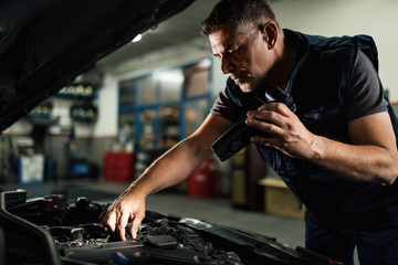Car mechanic using lamp while repairing engine in a workshop.