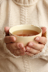 cup of hot fragrant tea in the hands of a woman, texture of a knitted sweater, close-up, copy space, concept of winter or autumn mood, photography for story, social media
