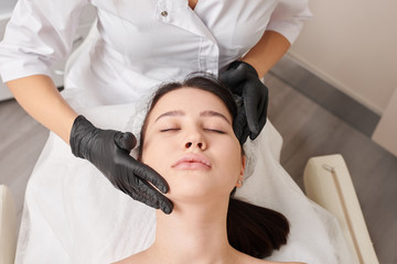 Spa concept. Young woman enjoying of facial massage in spa salon. Doctor in black gloves does facial massage to client in salon.