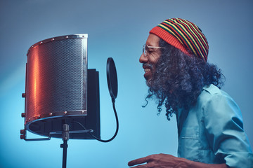 African Rastafarian singer male wearing a blue shirt and beanie emotionally writing song in the...