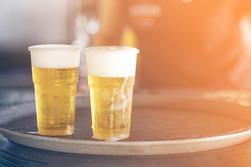 Two plastic glasses of beer on a tray. Two misted single-use plastic glasses with beer.