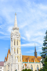 Fototapeta na wymiar Spire of the Matthias Church in Budapest, Hungary on a vertical photo. Roman Catholic church built in the Gothic style. Located in front of the Fisherman's Bastion in Buda Castle District