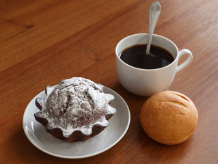 coffee mug, bun and chocolate cupcake on a small plate. On brown wooden background.