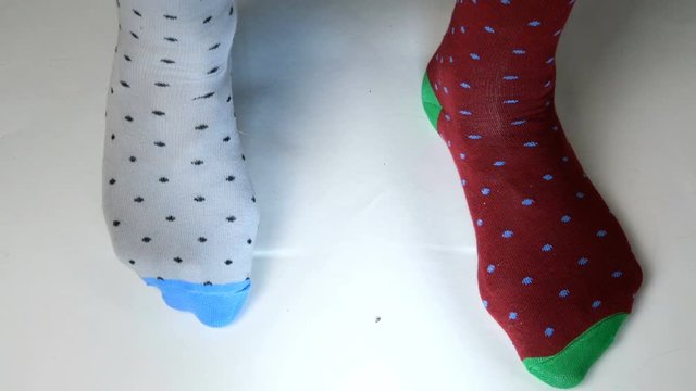 Human legs in fashionable socks of different colors move on white solid surface. Maybe he is dancing, doing sports or fitness. Close-up.