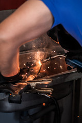 Car mechanic working on welding metal. Flying sparks