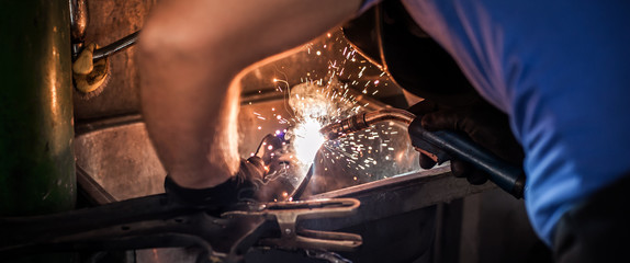 Car mechanic working on welding metal. Flying sparks