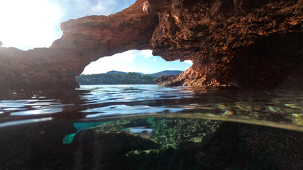 Underwater above and below photo of rocky seascape arch forming a beautiful emerald lagoon in tropical exotic island