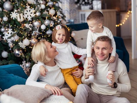 Christmas morning at home. happy family in white sweaters plays. real childhood. love warm care. Holiday New Year gifts living room decorated. mom dad daughter son siblings todlers young parents eve