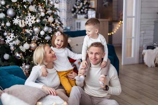 Christmas morning at home. happy family in white sweaters plays. real childhood. love warm care. Holiday New Year gifts living room decorated. mom dad daughter son siblings todlers young parents eve