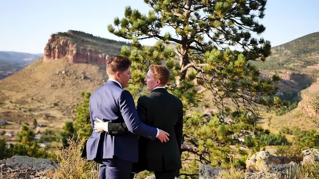 Slow motion shot from behind a newly married queer couple posing on the mountainside at their outdoor wedding