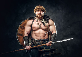 Severe barbarian in warrior clothes, posing on a dark background.