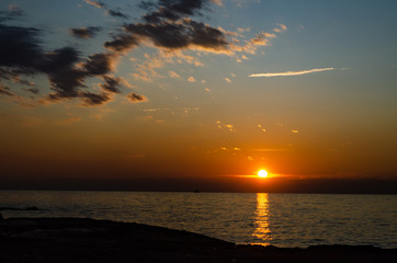 Fototapeta na wymiar Sunset on a beach with dramatic colours, sailboat, clouds and dark rocky beach