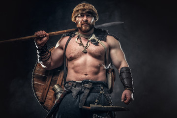 Fototapeta na wymiar Severe barbarian in warrior clothes, posing on a dark background.