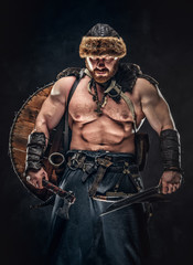 Severe barbarian in warrior clothes, posing on a dark background.