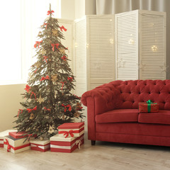 Gift boxes under decorated Christmas tree and red box with green riboon on Red sofa