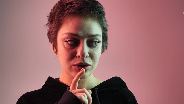 close-up female teenager puts his finger to his lips, a gesture of silence or secret against the background of neon. 4k