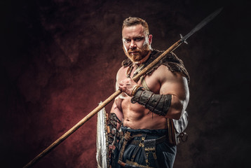 Fototapeta na wymiar Medieval warrior berserk holds a spear and shield. Posing on a dark background