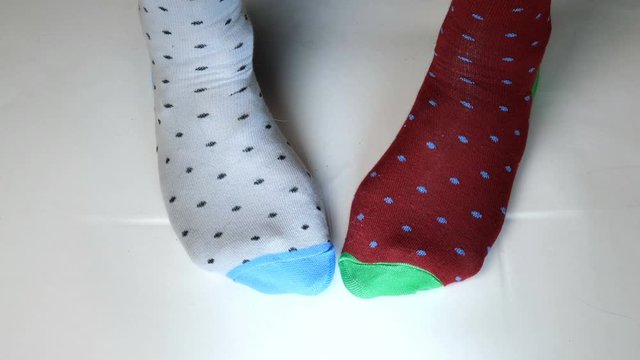 Human legs in fashionable socks of different colors move on white solid surface. Maybe he is dancing, doing sports or fitness. Close-up.
