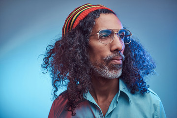 African Rastafarian male wearing a blue shirt and beanie. Studio portrait on a blue background.